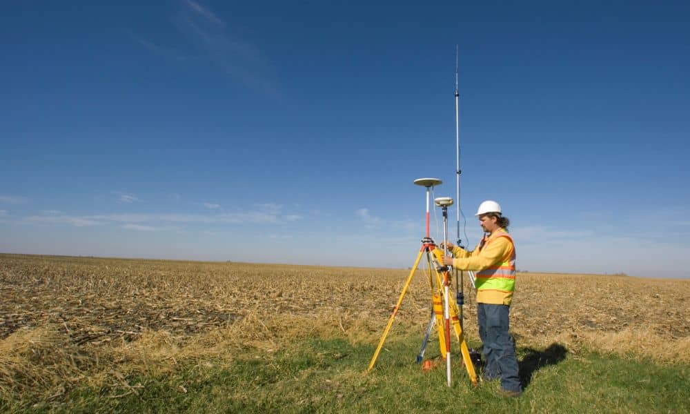 Land surveying professional using a GPS rover and tripod in an open field to capture accurate position data