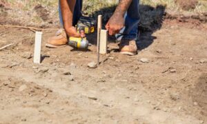A surveyor marking property lines during a boundary survey on a dirt lot