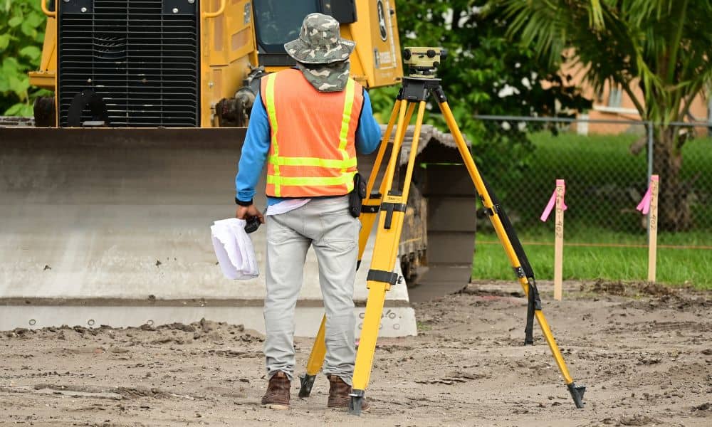  Surveyor conducting a boundary survey on a cleared urban site with safety gear and tripod equipment
