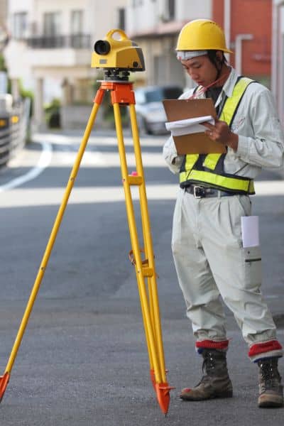 Land surveyor using equipment to measure boundaries during a property survey on a residential street
